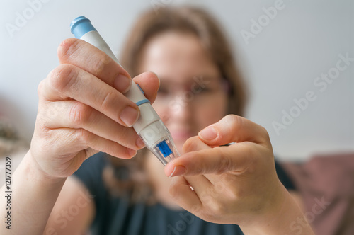 Woman is using needle for glucose level test with glucometer. photo