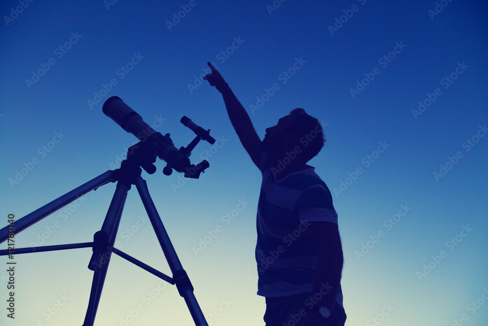 Man looking at the night sky with telescope beside him.
