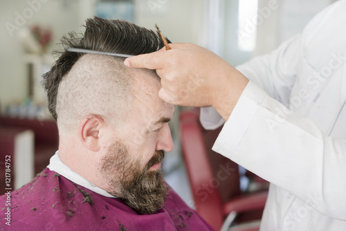 Barber makes a mohawk hairstyle of a adult bearded man