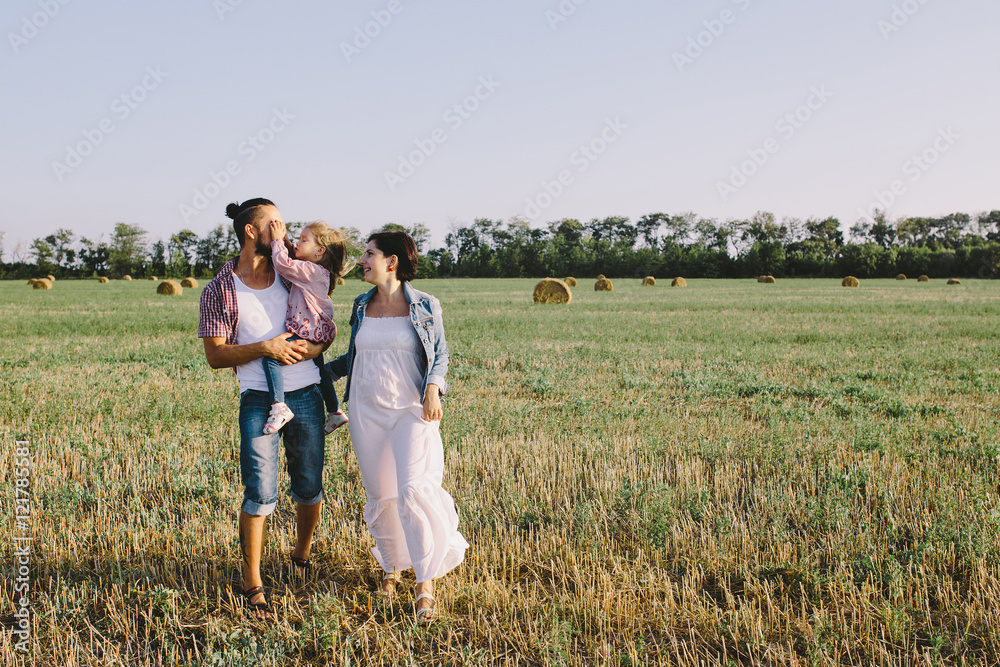 father in a red plaid shirt, daughter and pregnant mother in white dress enjoying life outdoor in field father in a red plaid shirt, daughter and pregnant mother in white dress enjoying life outdoor in field