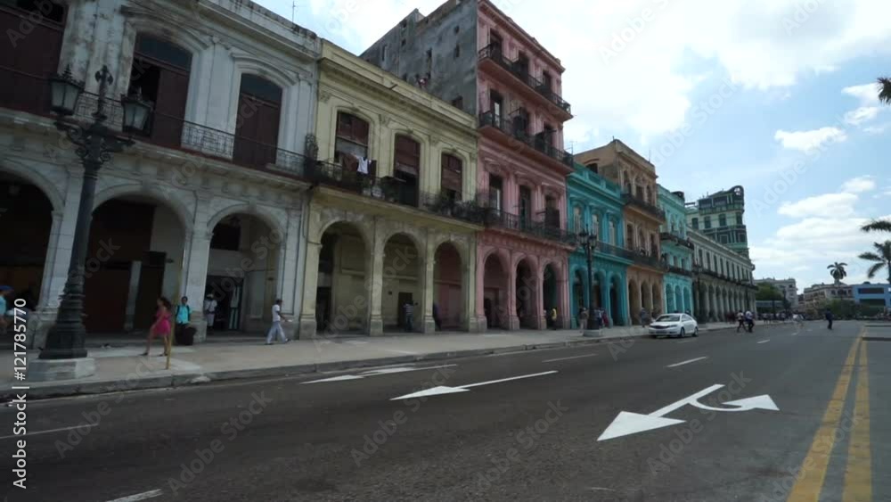 Central touristic street in Havana of multi-colored houses with big arches. Bright colorful retro cars are passing by at summer sunny day. Central touristic street in Havana of multi-colored houses with big arches. Bright colorful retro cars are passing by at summer sunny day.
