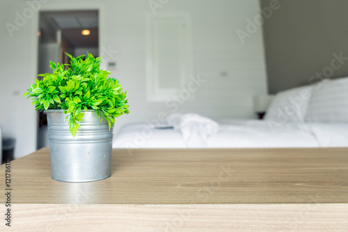 Wooden table with vintage vase plastic plant on blur bedroom