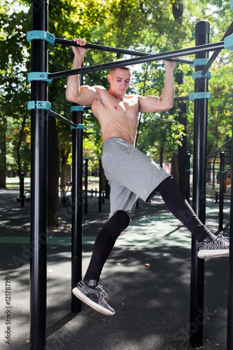 Young man doing pull ups on horizontal bar outdoors, workout, sp