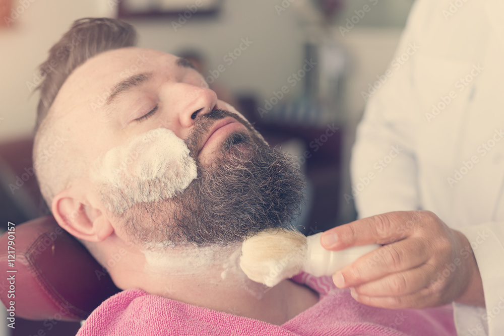 Client with foam on face during beard shaving in barber shop. Toned Client with foam on face during beard shaving in barber shop. Toned