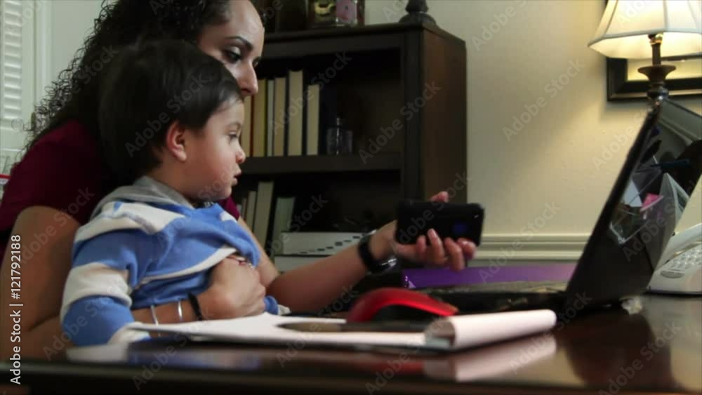 A pretty Hispanic mom working in her home office takes a call on her cell phone while caring for her little son who is sitting in her lap. A pretty Hispanic mom working in her home office takes a call on her cell phone while caring for her little son who is sitting in her lap.