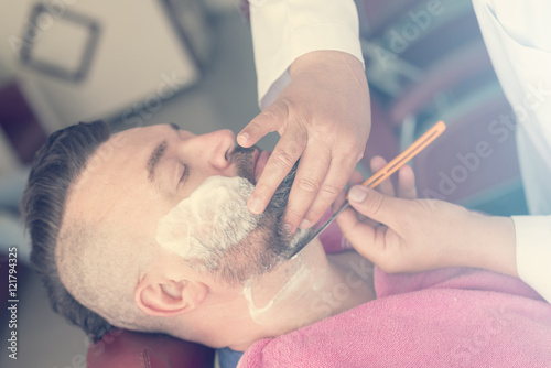 Client with foam on face during beard shaving in barber shop. Toned photo