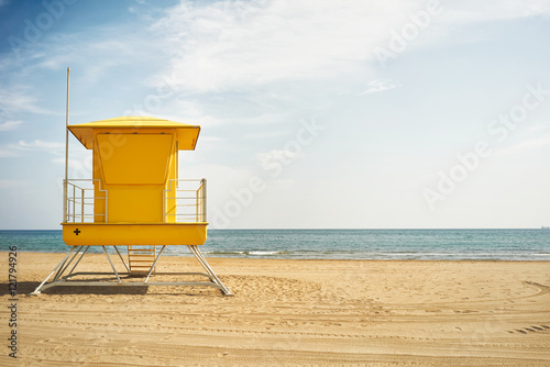 Quiet blue sky and sea and a saturated yellow lifeguard post on a deserted beach in beautiful weather