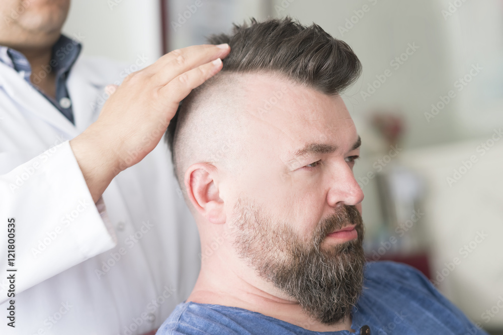 Obraz premium Barber robi fryzurę irokezowi u dorosłego mężczyzny z brodą