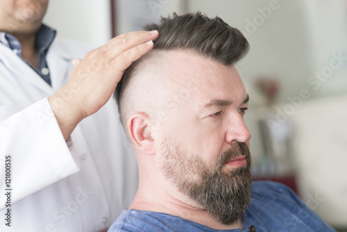 Barber makes a mohawk hairstyle at the adult man with beard