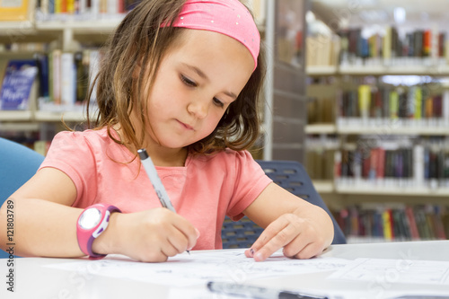 young caucasian child girl drawing on library background