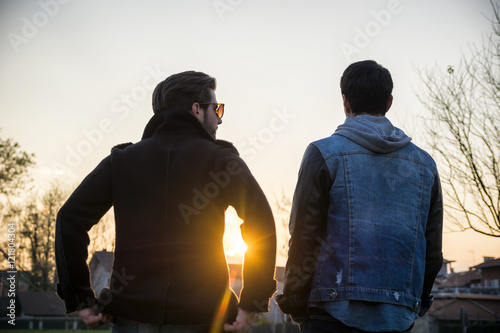 Two handsome casual trendy young men, 2 friends, in an urban park walking and chatting together