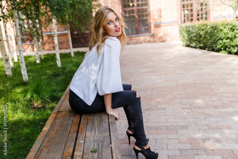 Blonde woman in ripped jeans sitting on park bench Stock Photo | Adobe ...