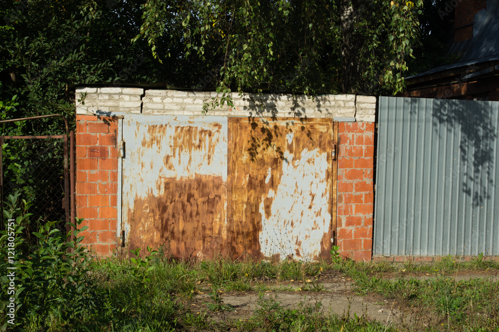 Garage building with rusty doors. Greens and shadow around him. Garage building with rusty doors. Greens and shadow around him.