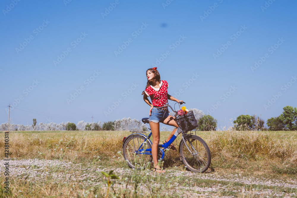 Young pinup woman cycling in fields under bright blue summer sky copy space image Young pinup woman cycling in fields under bright blue summer sky copy space image