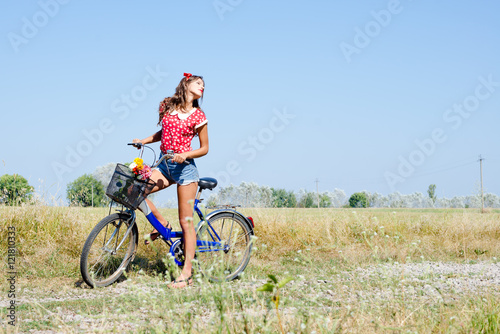 Young pinup woman cycling in fields under bright blue summer sky copy space image