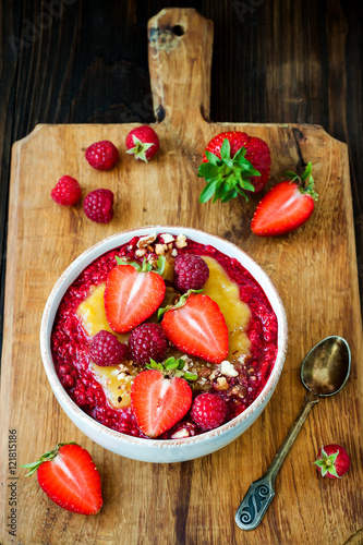 Healthy breakfast. Mango maca smoothie bowl topped with hazelnuts, oat granola, fresh berries and raspberry puree. Rustic style, vintage silverware.