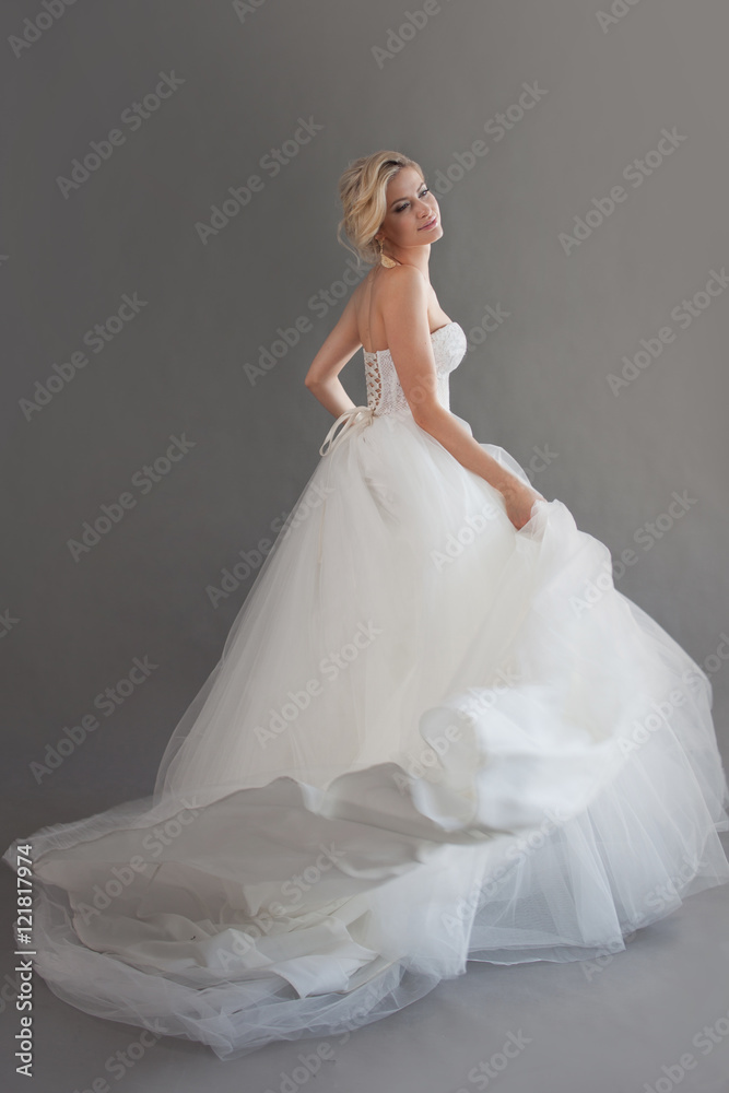 Charming young bride in luxurious wedding dress. Pretty girl in white. Emotions of happiness, gray background Charming young bride in luxurious wedding dress. Pretty girl in white. Emotions of happiness, gray background