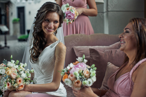 Bride is smiling to the bridesmaid with a bouquet