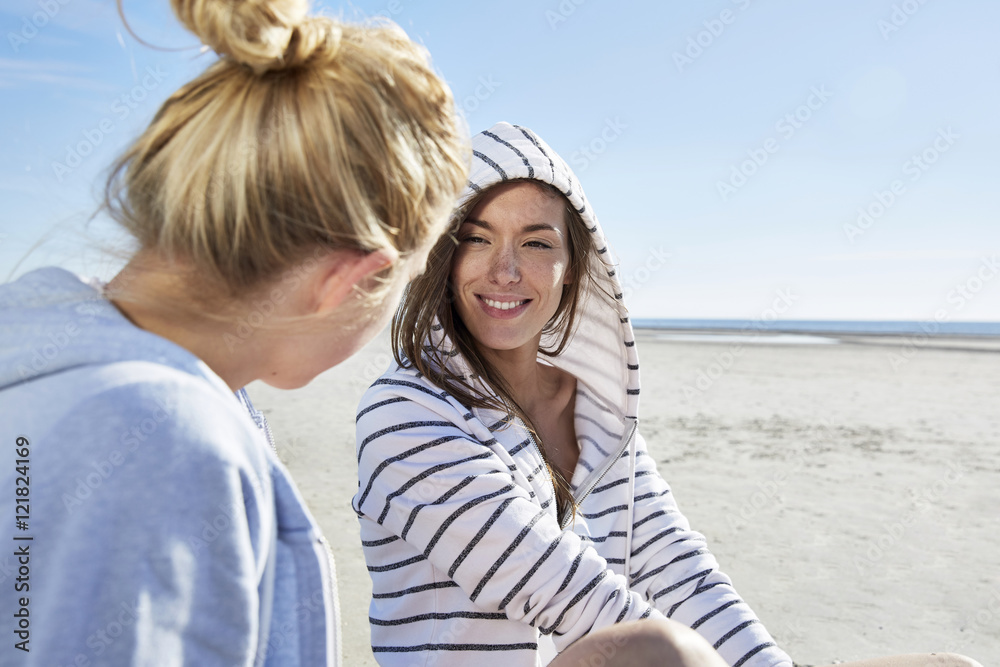 Two female friends wearing hoodies sitting on the beach Two female friends wearing hoodies sitting on the beach