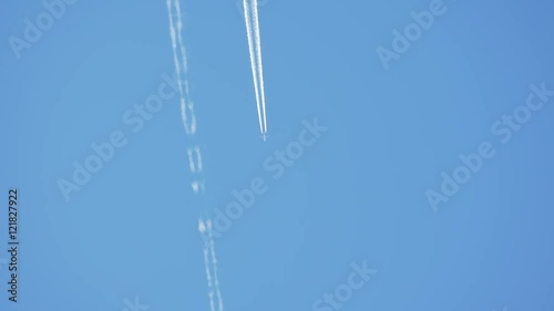 Airplane passes across clear blue sky leaving a jet contrail. Slow motion. photo