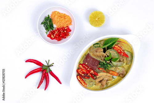 Green chicken curry in coconut milk s with side dish as minced dried shrimp sliced red chili sliced kaffir lime leaves and green lemon on white background.