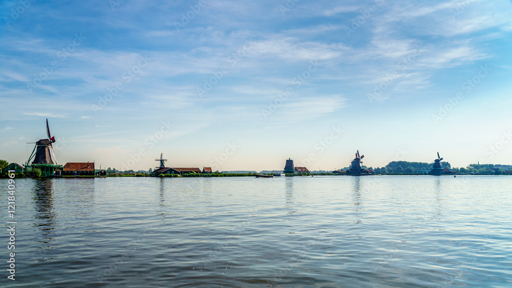 View from the Zaan River of old Dutch Windmills and historic houses along the river at the historic villages of Zaanse Schans and Zaandijk in the Netherlands