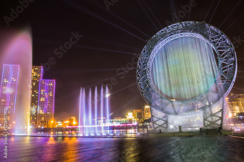 Astana, Kazakhstan. Musical sun fountain show in Ishim river embankment with buildings on background