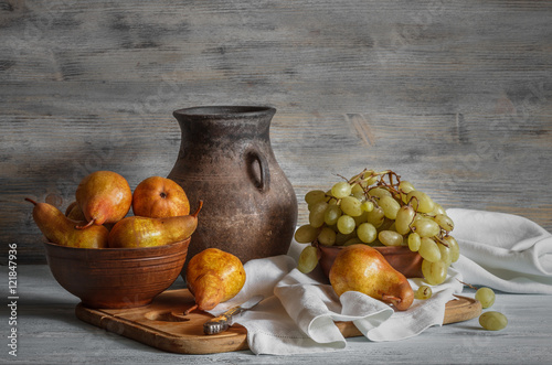 Still life in a rustic style: a set of clay dishes, grapes and pears on a wooden table. Natural light from the windows.
