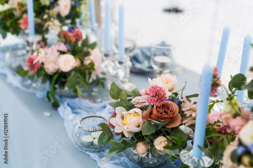 Fototapeta Naklejka Na Ścianę i Meble -  Dinner table decor. Blue candles surroun rose bouquets