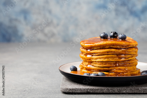 Pumpkin pancakes with maple syrup and blueberries on a plate. Grey stone background Copy space