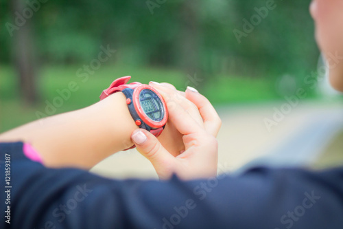 Ftitness girl checks stopwatch tracker on her wrist during runni photo