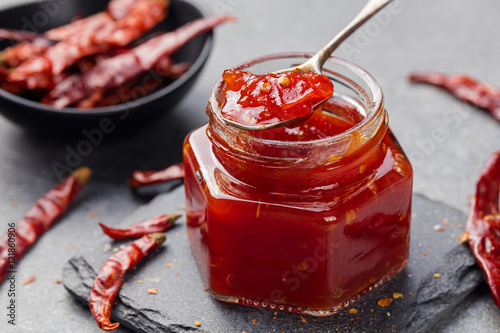 Tomato and chili sauce, jam, confiture in a glass jar on a grey stone background photo