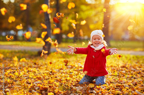 happy child girl laughing and playing  leaves in autumn