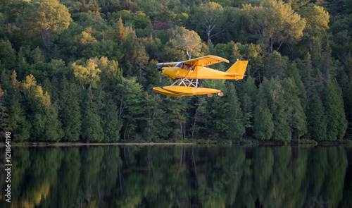 Small yellow airplane on pontoons comes in for a landing on an Eastern Ontario lake on a summer's evening.
