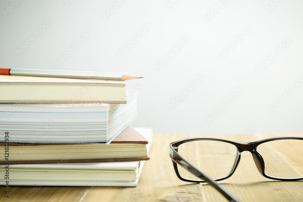 Eyeglasses, books and pencil on wood table, selective focus
