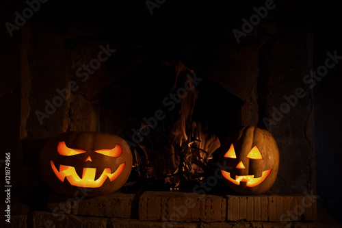 two Halloween pumpkins at the fireplace with fire in dark with y