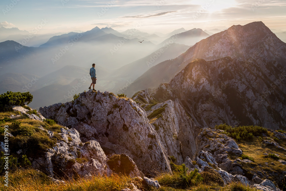 Fototapeta premium Człowiek stojący na szczycie góry o zachodzie słońca