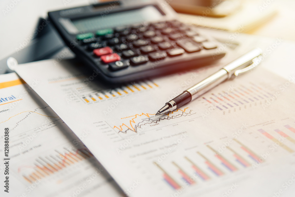 Pen on financial documents with calculator in background with sunlight filter. Pen on financial documents with calculator in background with sunlight filter.
