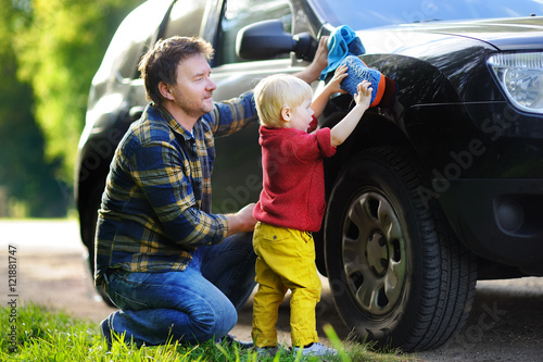 Father with his toddler son washing car together © Maria Sbytova