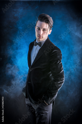 Young businessman confidently posing and looking at camera, wearing suit, on dark background