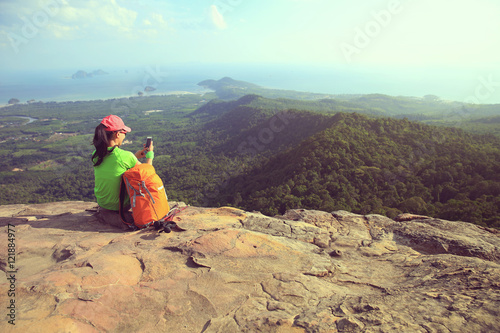 young woman hiker taking photo with smartphone on mountain peak cliff