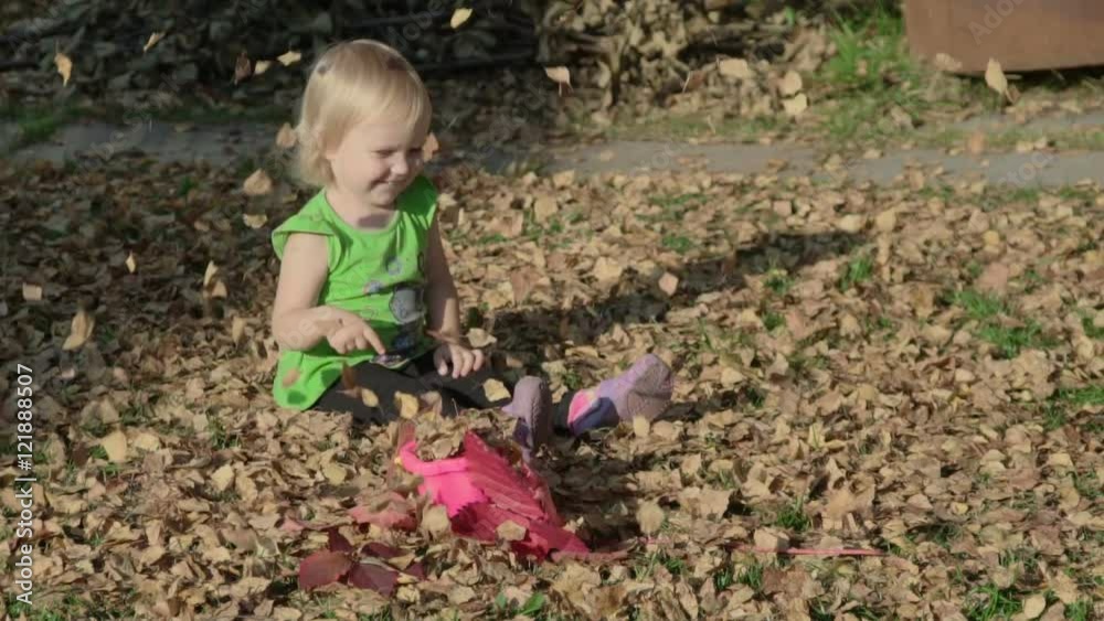 Cute baby girl playing with leaves in autumn