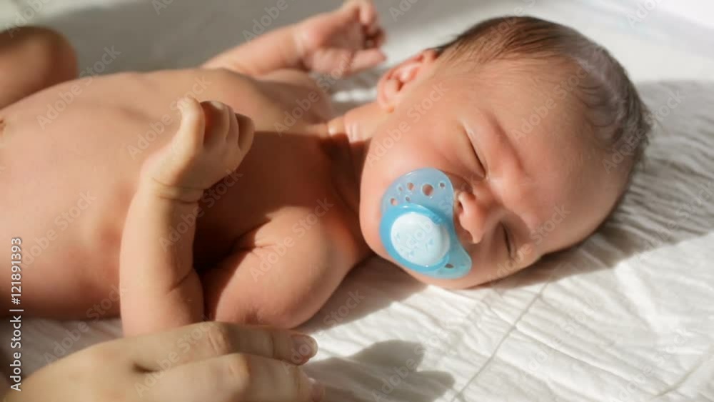 Closeup shot of mother giving soother to hew newborn baby son lying on bed in sun rays Closeup shot of mother giving soother to hew newborn baby son lying on bed in sun rays