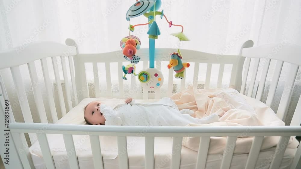 Cute 3 months old baby playing with mobile in white wooden crib