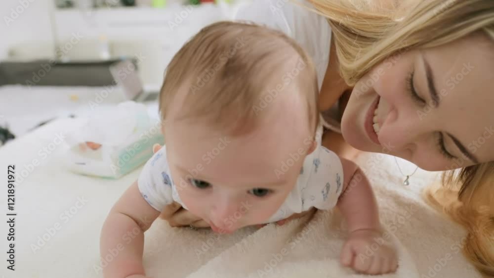 Closeup shot of cute 3 months old baby boy crawling on bed with his beautiful young mother Closeup shot of cute 3 months old baby boy crawling on bed with his beautiful young mother