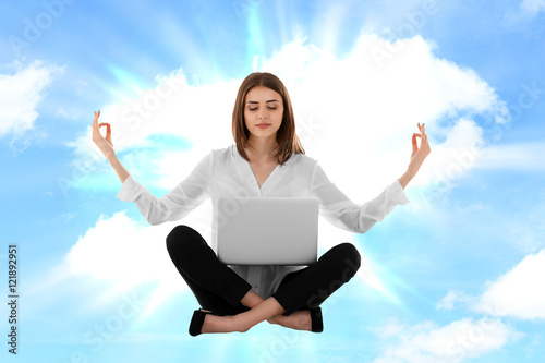 Businesswoman with laptop sitting in lotus pose against sky background. Yoga concept. © Africa Studio