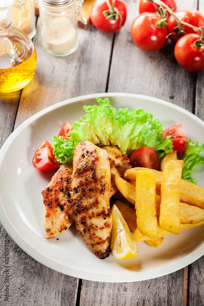 Grilled chicken breasts served with fries and fresh salad Grilled chicken breasts served with fries and fresh salad