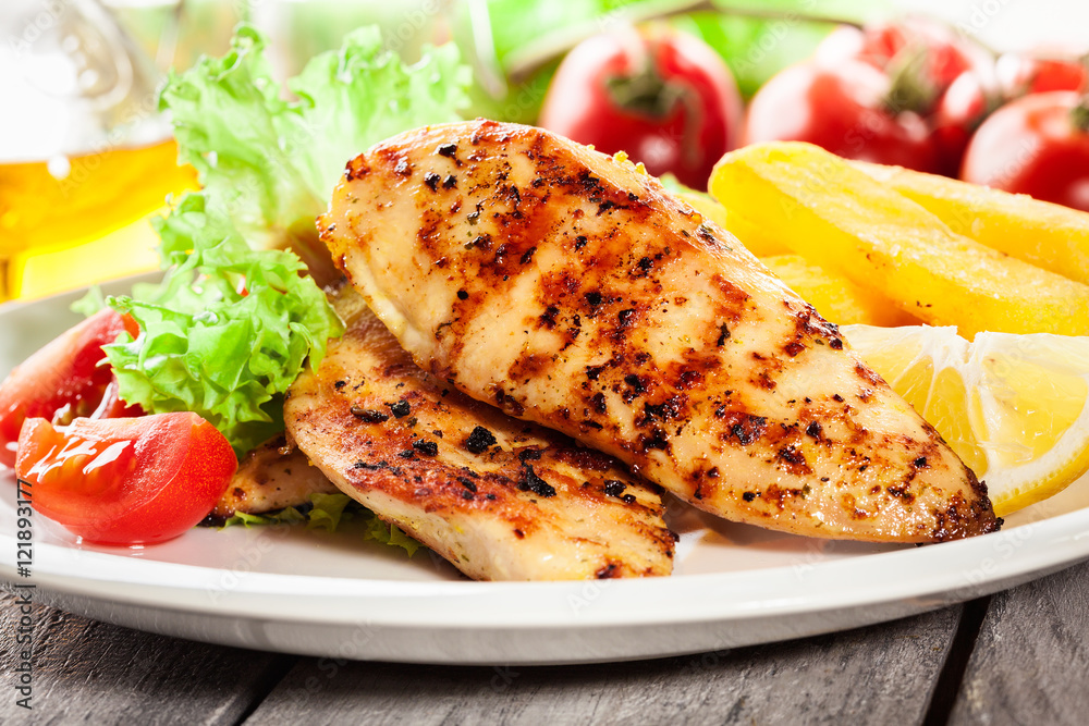 Grilled chicken breasts served with fries and fresh salad Grilled chicken breasts served with fries and fresh salad
