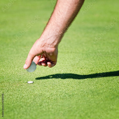 Golfer placing golf ball on the green