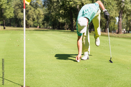 Golfer placing golf ball on the green © Microgen